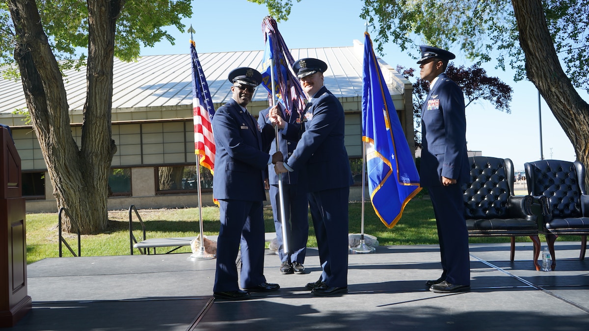 photo of USAF Airmen standing on a stage, two Airmen are holding a unit flag in between them
