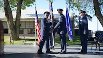 photo of USAF Airmen standing on a stage, two Airmen are holding a unit flag in between them