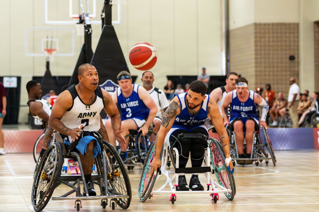 A soldier and an airman in wheelchairs race for a loose ball during a basketball game, as other players in the background look ready for the next play.