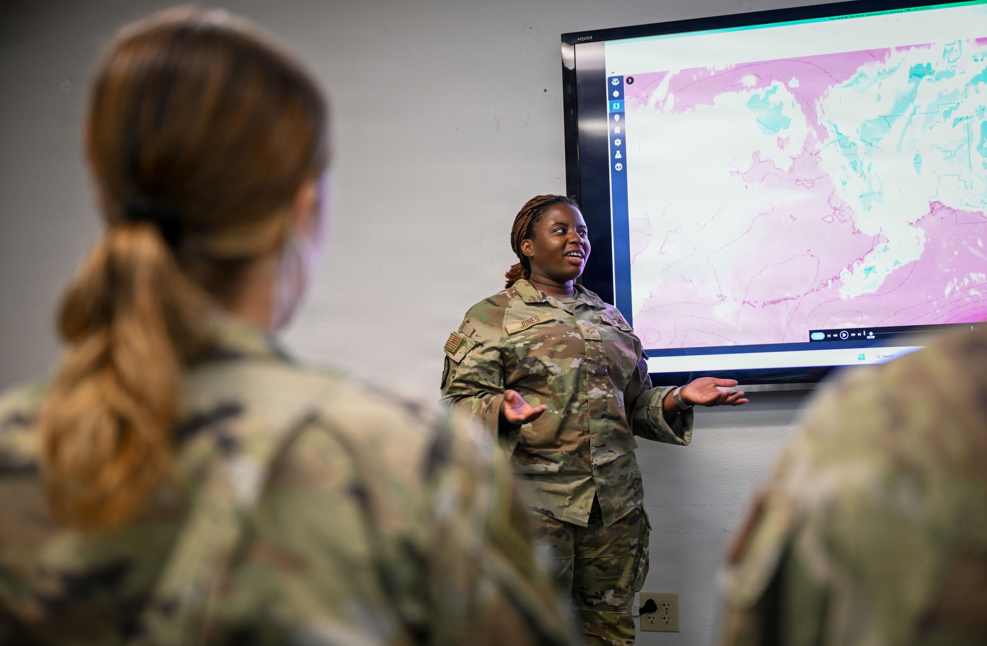 An Airman speaks in front of a screen depicting satellite imagery of Alaska