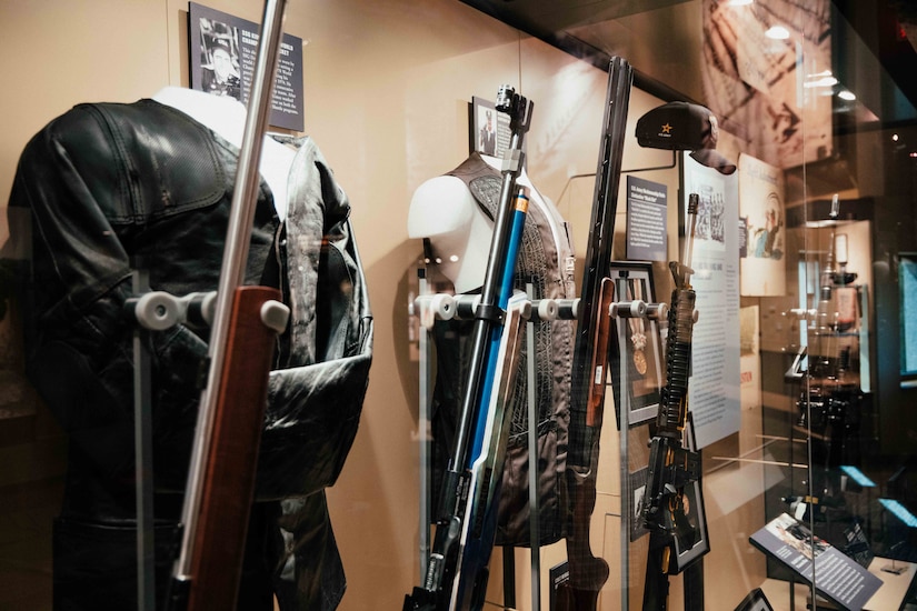 Old uniforms and rifles are on display inside a glass case.