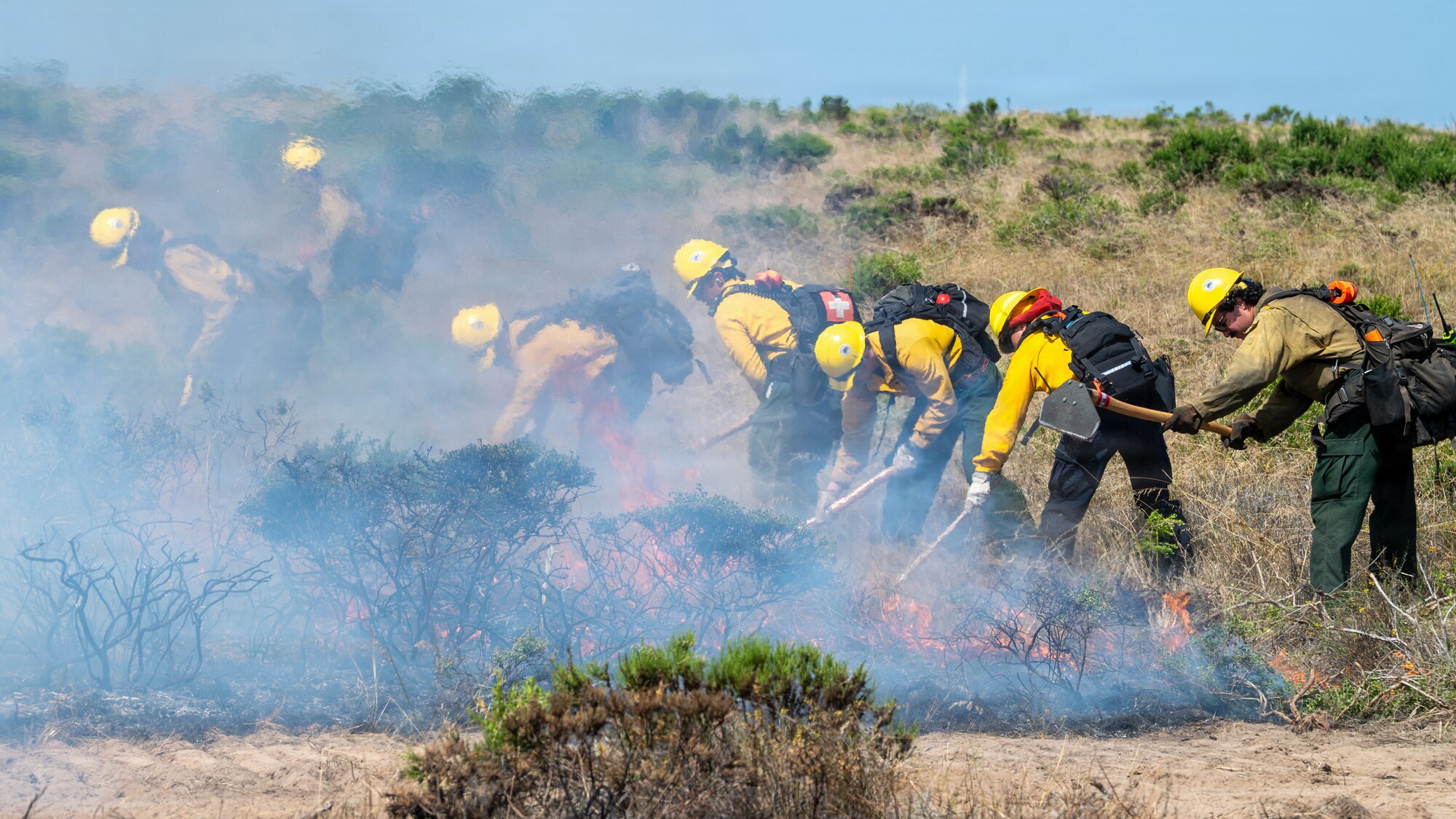 A group of people dig into the ground around an active fire