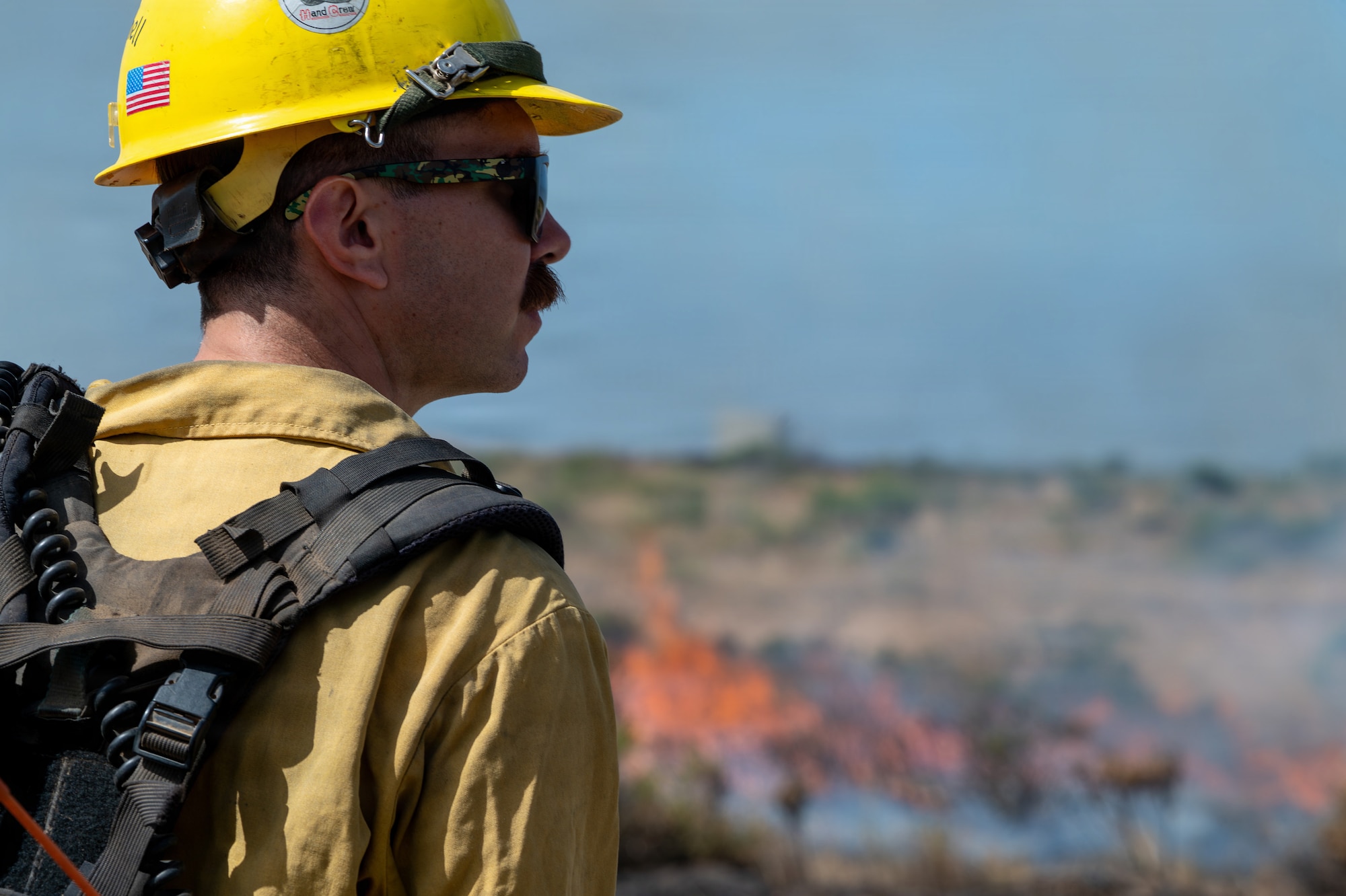 A person looks to their right as fire grows in the background