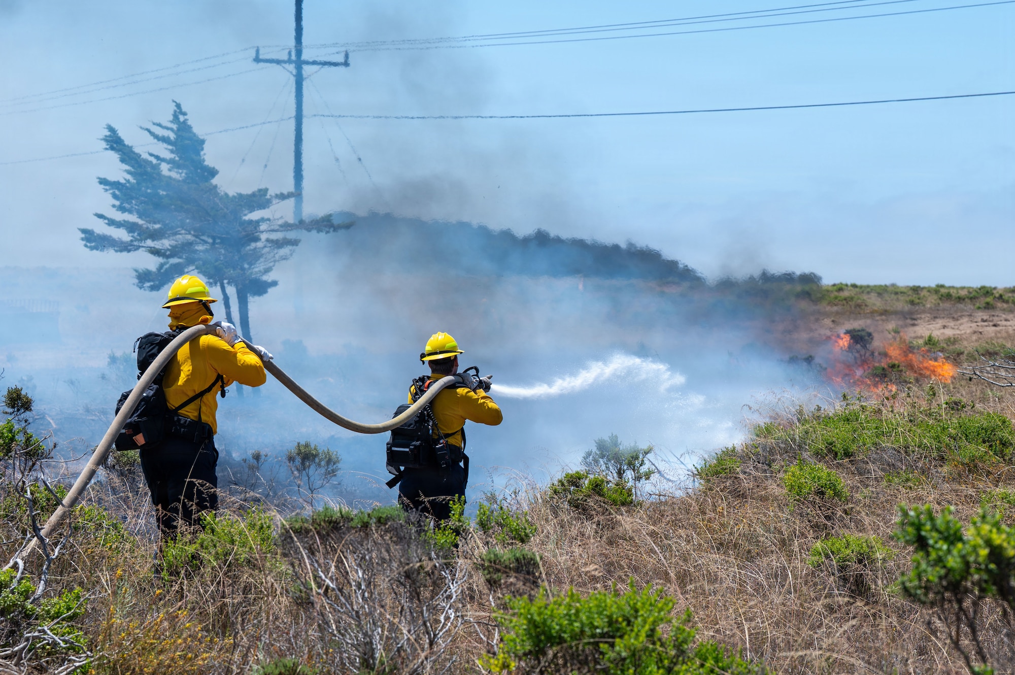 Two people hold a hose outside.