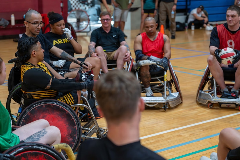 Nearly a dozen people in athletic attire sit in wheelchairs while gathering in a circle inside a gym.