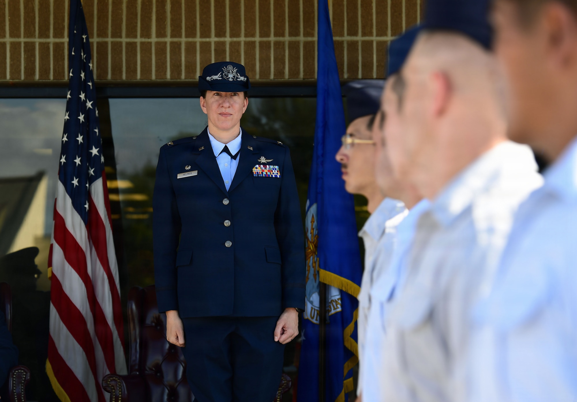 A woman in U.S. Air Force uniform stand at attention as Airmen pass.