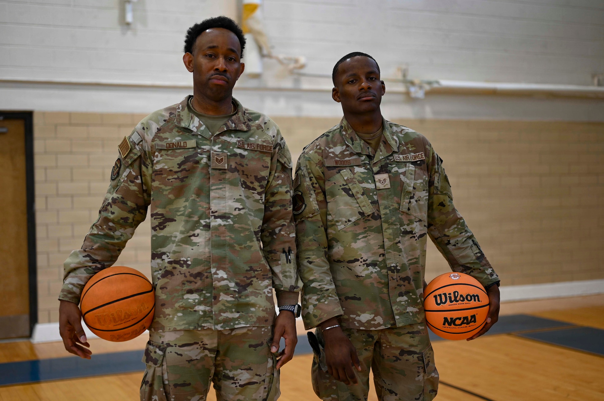 Two uniformed members pose for a photo on a basketball court.