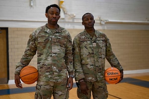Two uniformed members pose for a photo on a basketball court.