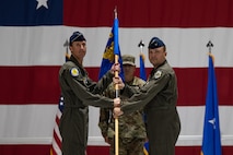 Brig. Gen. Lawrence Sullivan, right, outgoing 57th Wing commander, passes the guidon to Maj. Gen. David Epperson, left, U.S. Air Force Warfare Center commander, in front of Chief Master Sgt. Jeremy Miller, center, the 57th Wing command chief, during a change of command ceremony at Nellis Air Force Base, Nevada, June 15, 2026.