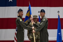 Brig. Gen. David Epperson, left, U.S. Air Force Warfare Center commander, passes the guidon to Col. Scott Mills, right, incoming 57th Wing commander, in front of Chief Master Sgt. Jeremy Miller, center, the 57th Wing command chief, during a change of command ceremony at Nellis Air Force Base, Nevada, June 15, 2026.