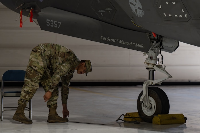 An Airman takes off a name tape from an F-35 Lightning II aircraft and places the magnet on the floor.