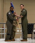 Three USAF Airmen stand on a stage, two Airmen hold a unit flag in between them