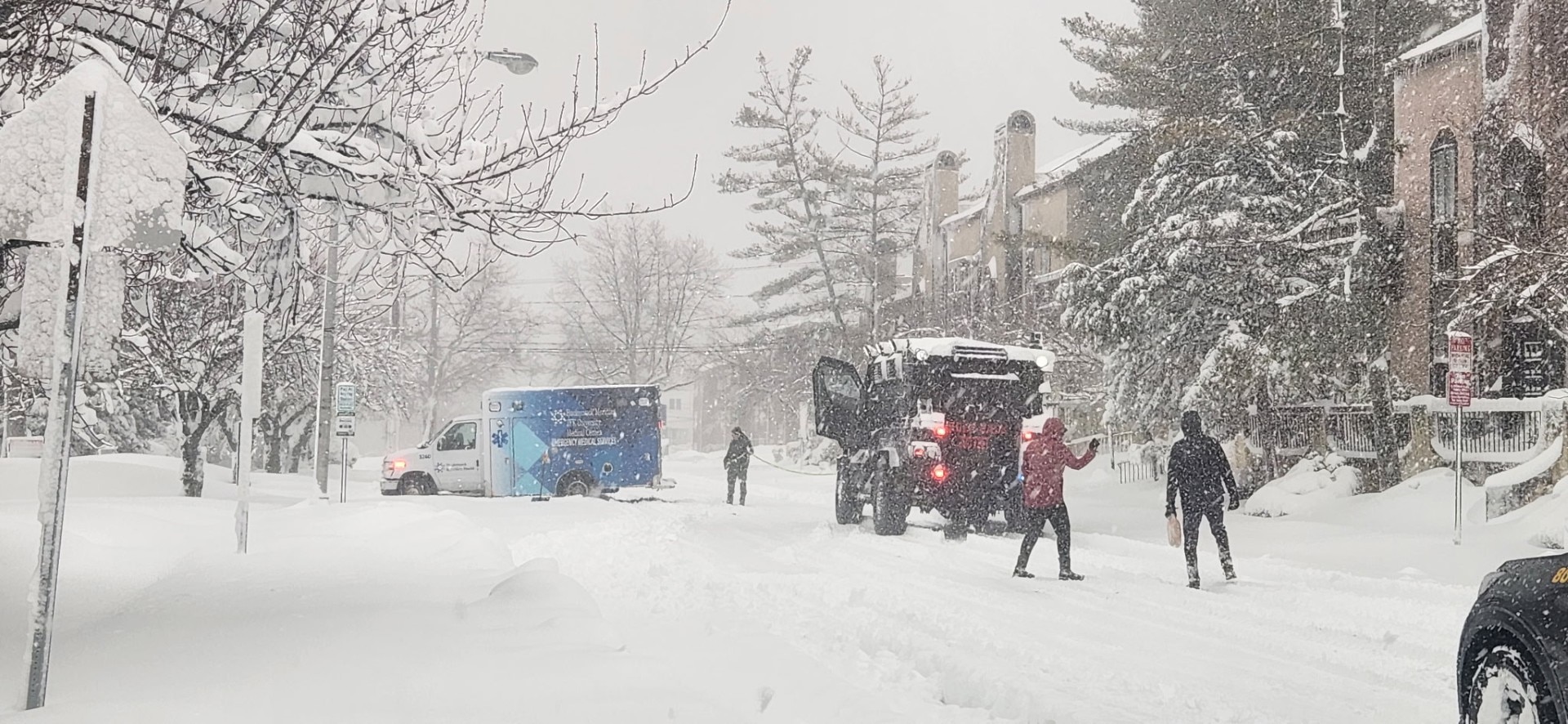 A military vehicle is used to get an ambulance out of a snowbank.