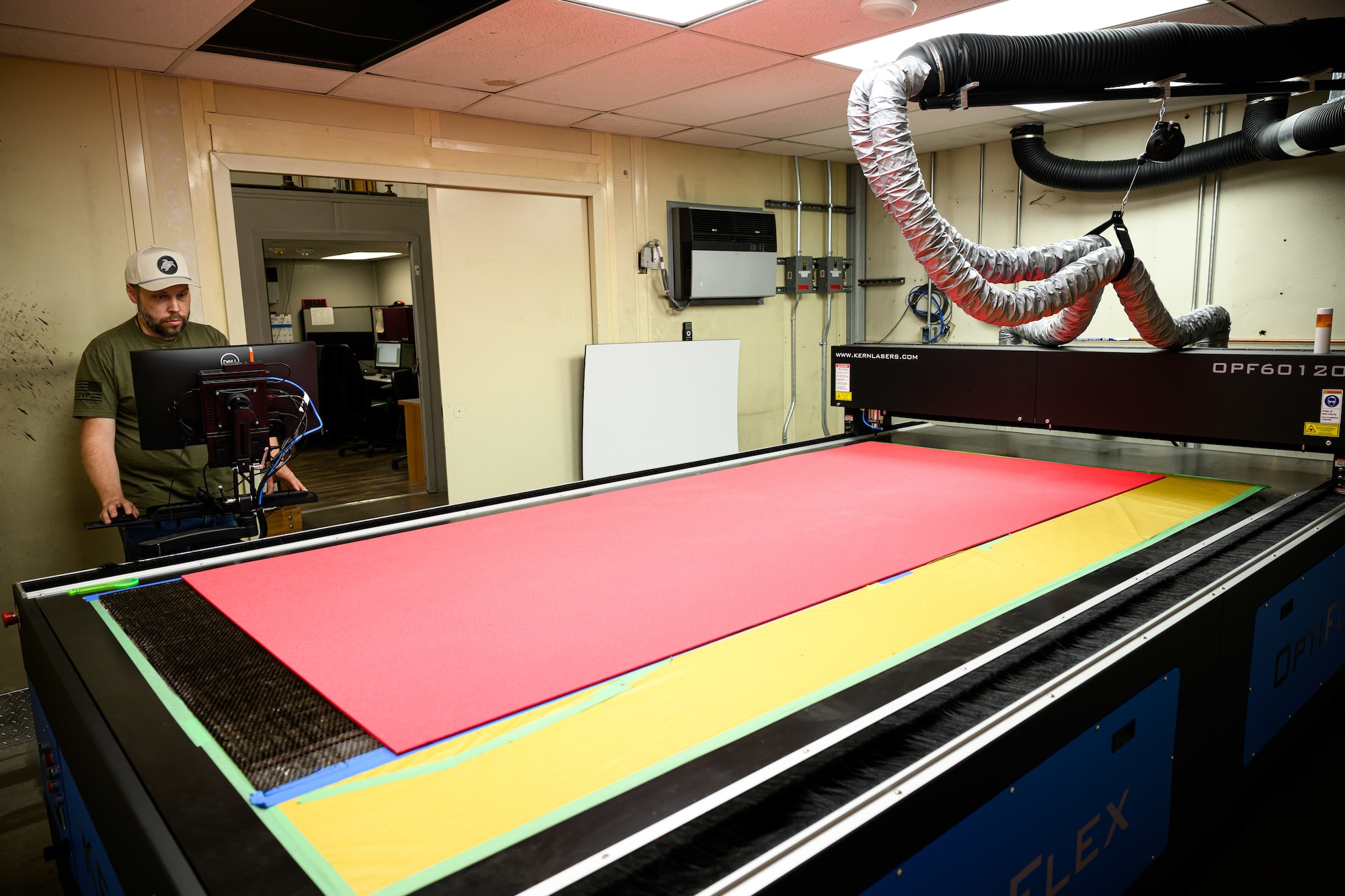 Daniel Parker looks at a computer screen while a sheet of red foam sits ready on top of a cutting machine.