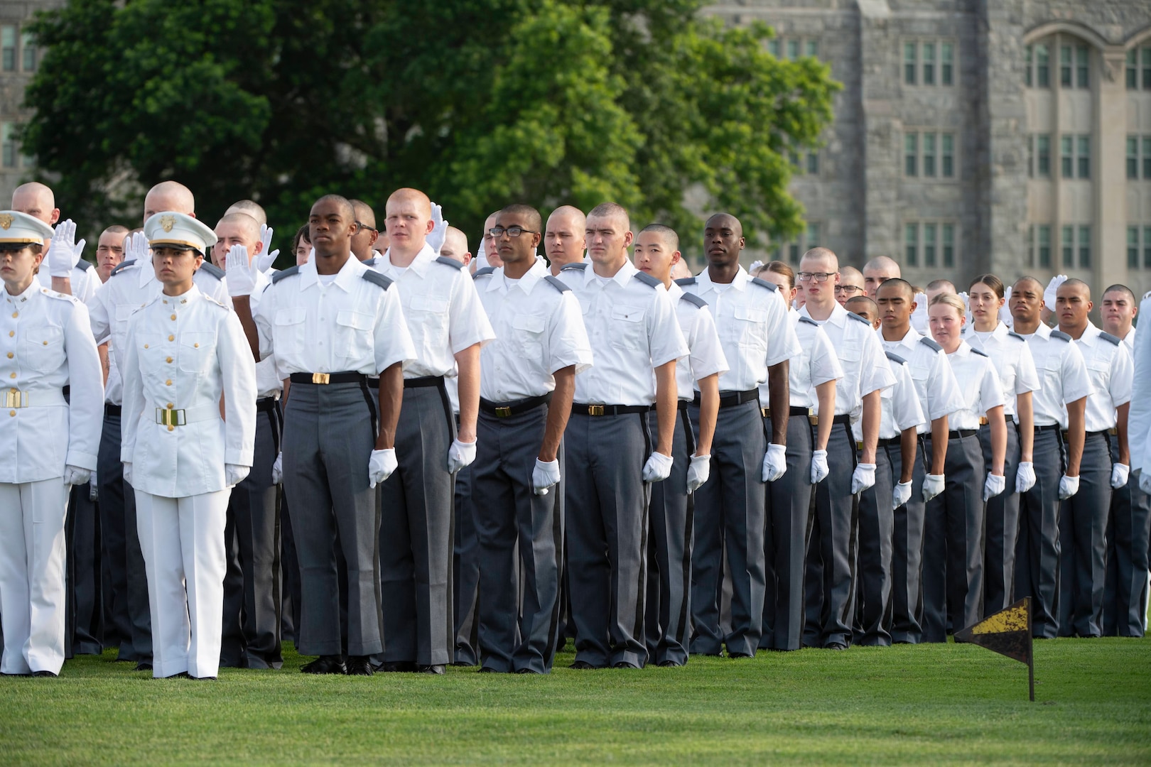 Army cadets stand in line formation in dress uniforms on field