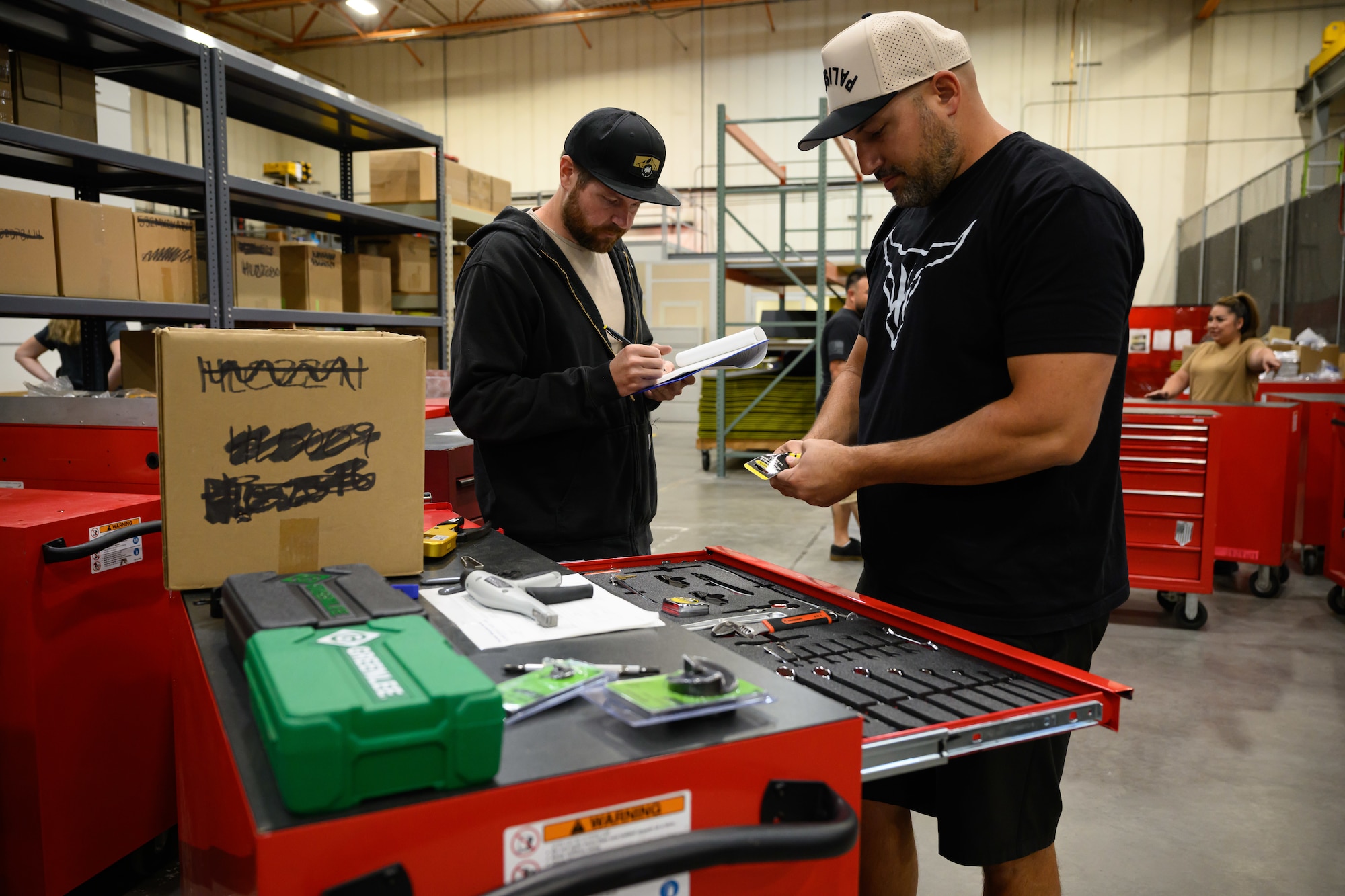 Trevor Goff stands writing in a notebook while Zane Johnson inspects tools over the open drawer of a toolbox