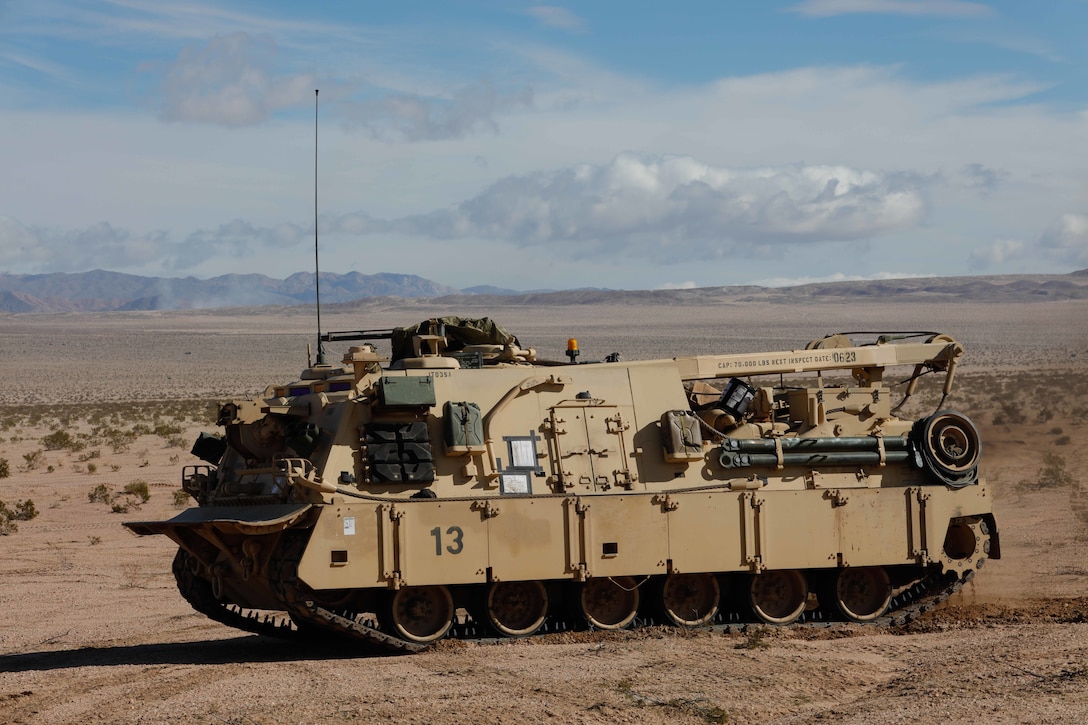 A large tan combat vehicle maneuvers in a desert setting.