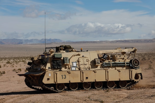 A large tan combat vehicle known as the M88 Hercules maneuvers in a desert setting.