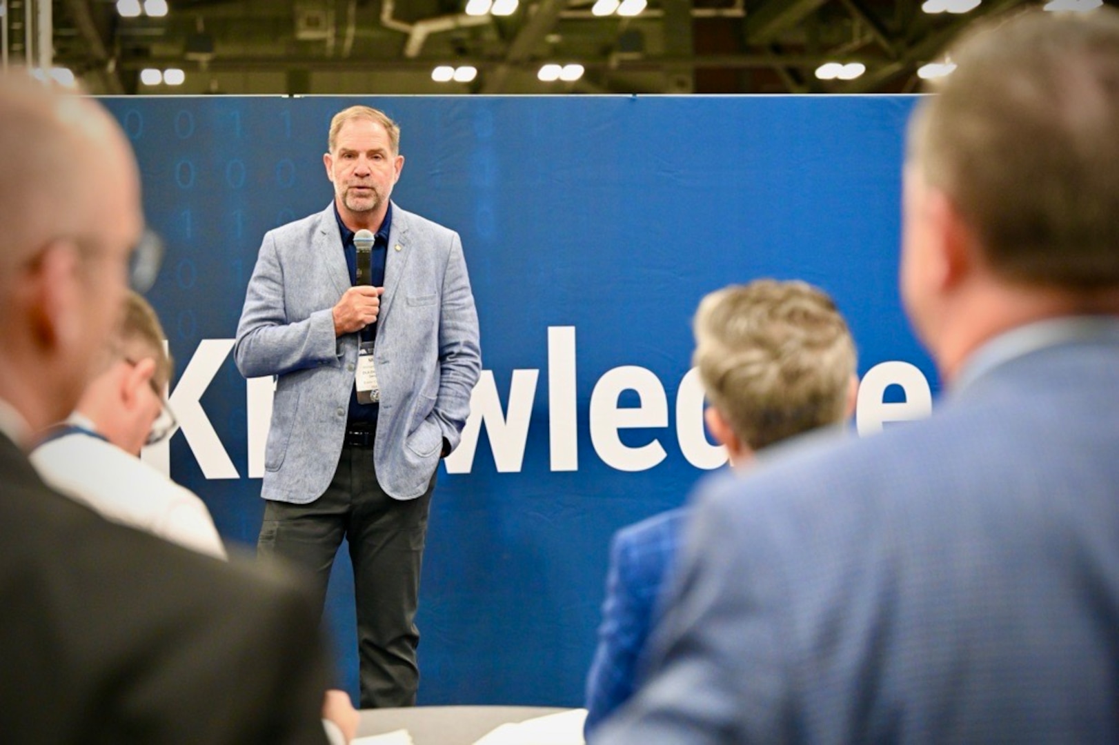 A man stands holding a microphone as he takes questions from the audience.