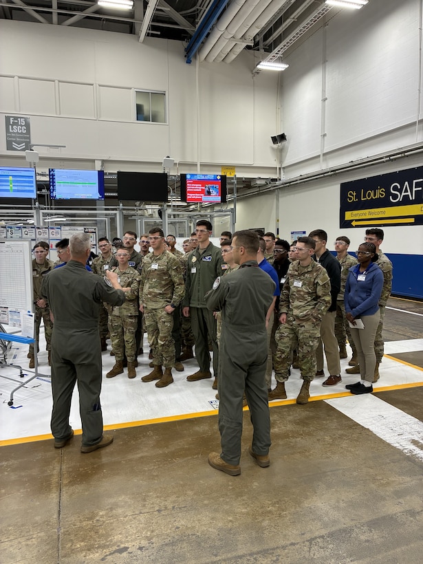 A group of men and women wearing military uniforms have a discussion on a factory floor