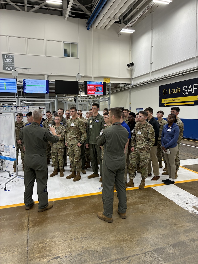 A group of men and women wearing military uniforms have a discussion on a factory floor