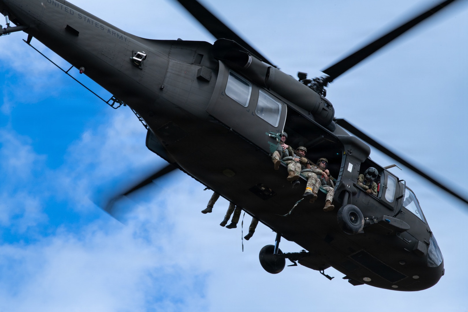 Three soldiers sit by an open door of a helicopter taking off.