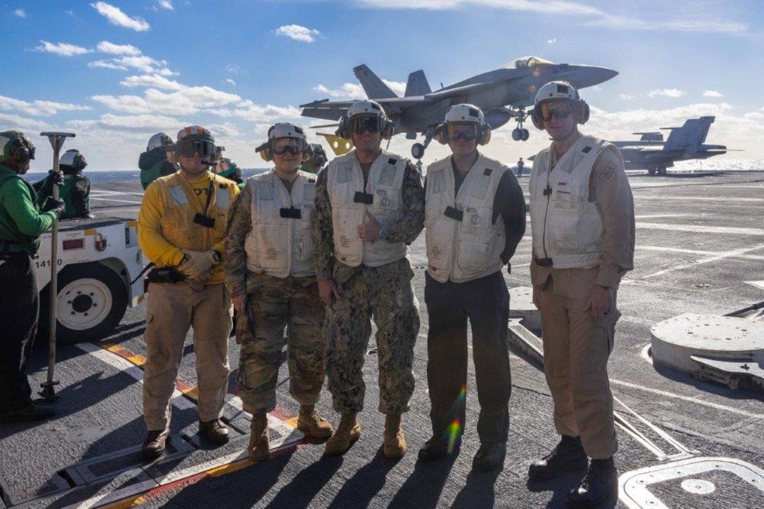 A group of people stand in front of an aircraft carrier.