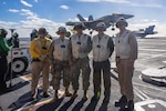 A group of people stand in front of an aircraft carrier.