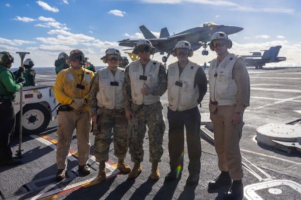 A group of people stand in front of an aircraft carrier.