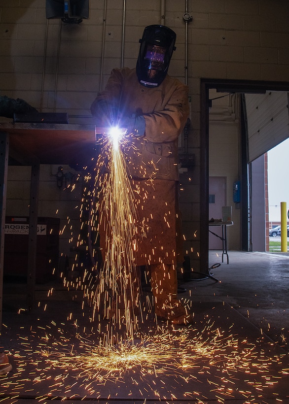 A person wearing a welding mask sends sparks flying to the floor.