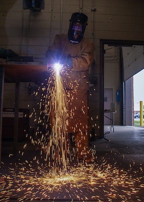 A person wearing a welding mask sends sparks flying to the floor.