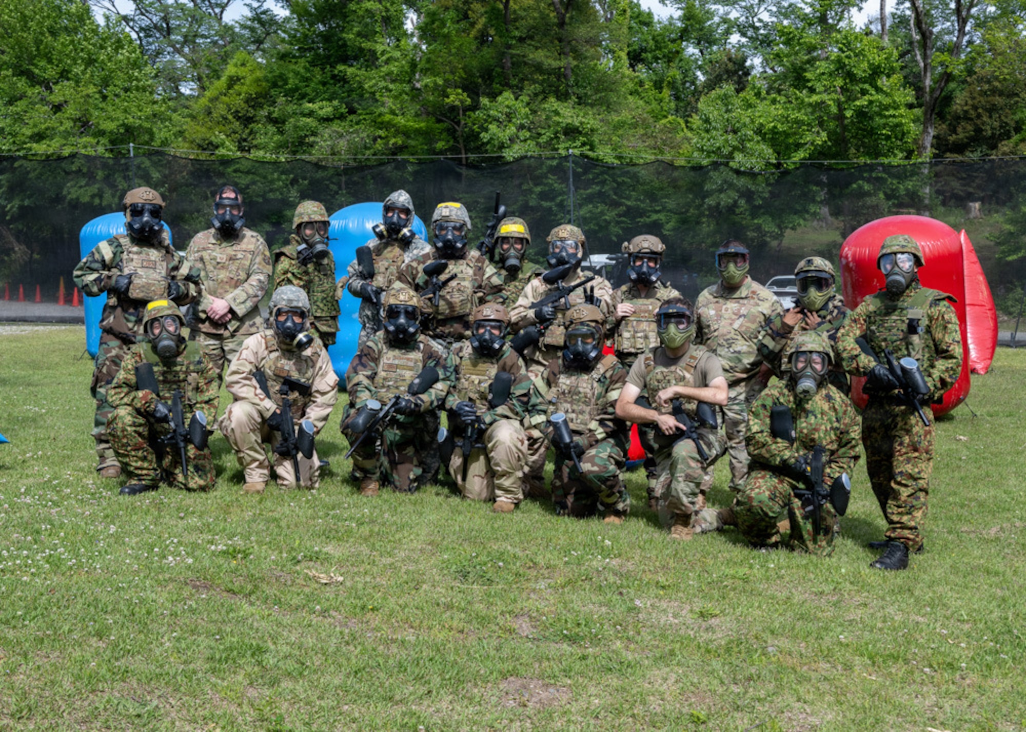 Military members with gas masks and camouflage NBC pose with paintball guns.