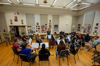 A student wind ensemble sits in a semicircle around the conductor.