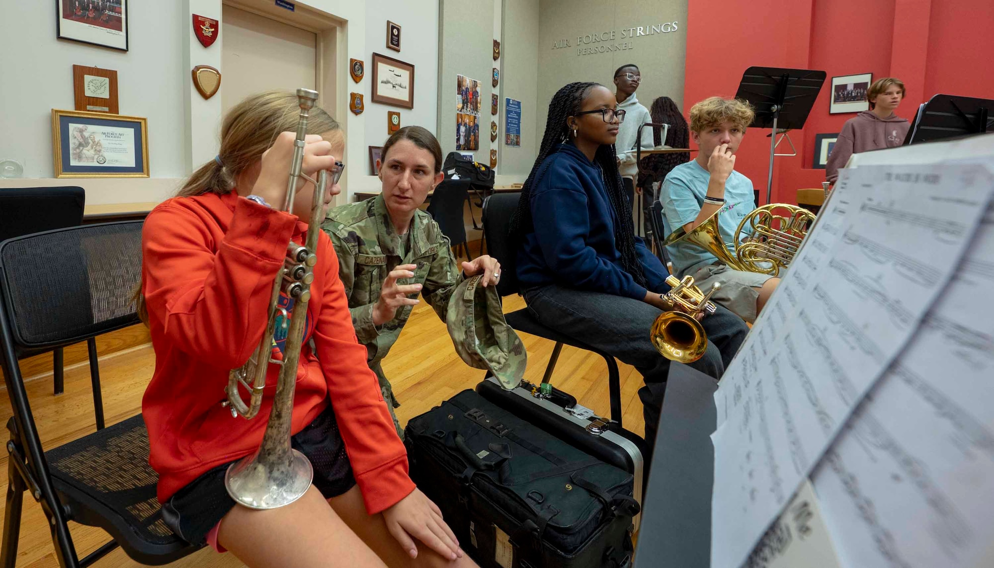 An Airman crouches next to a student holding a trumpet.