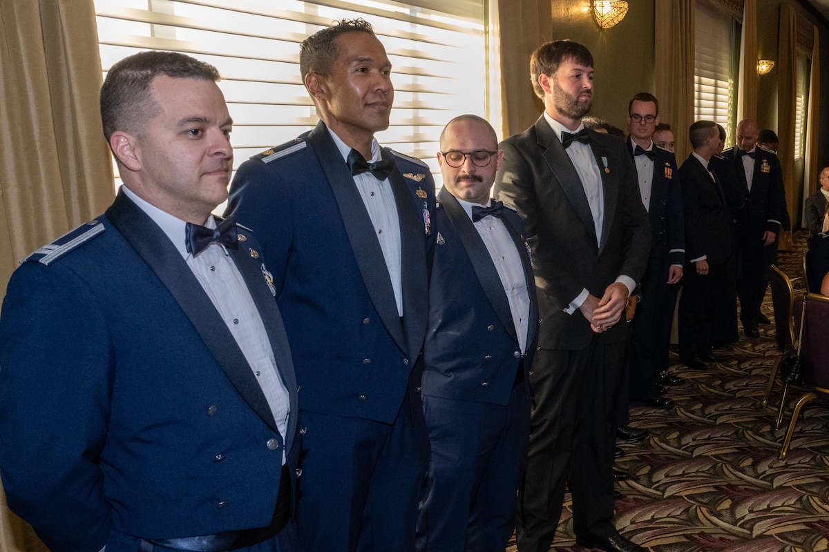 AQIC graduates stand lined up against the wall. They are wearing their mess dress uniforms.