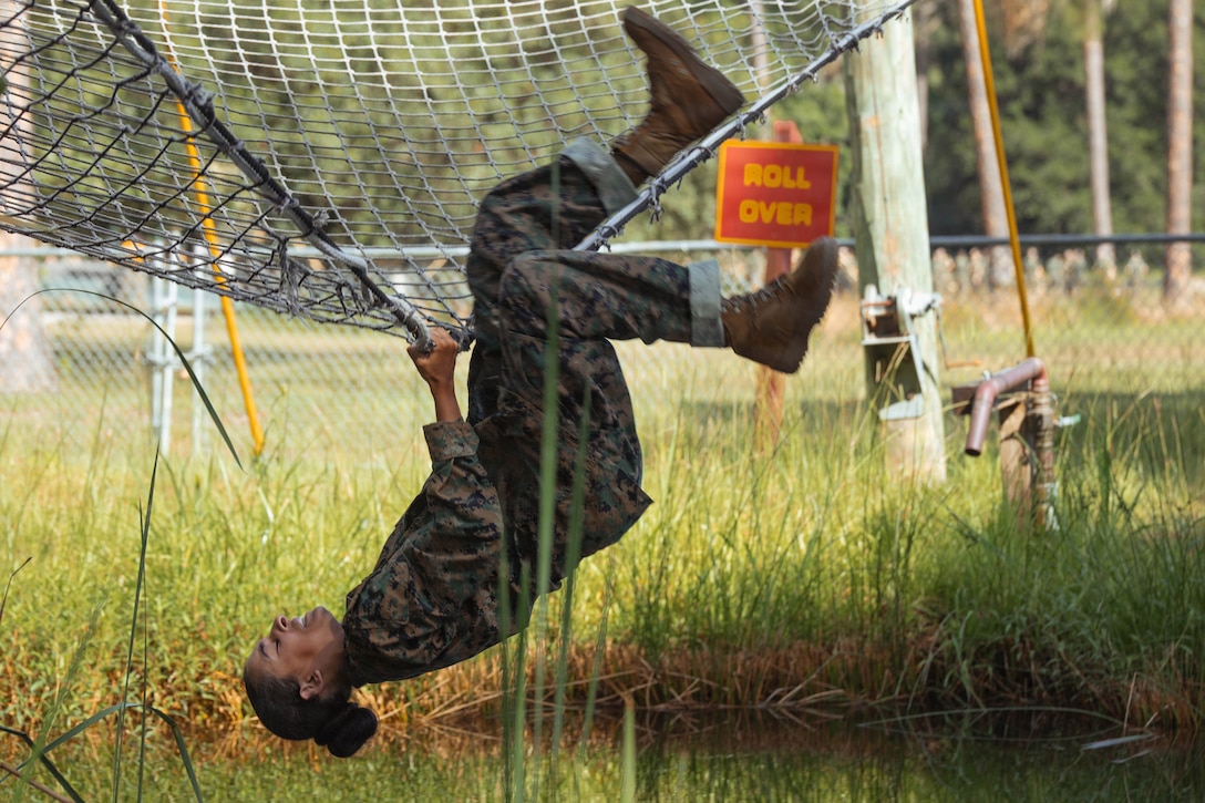 A Marine hangs nearly upside down from a net in a field.