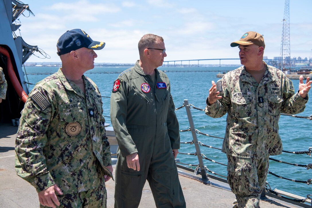 Three military men walk on the deck of a destroyer.