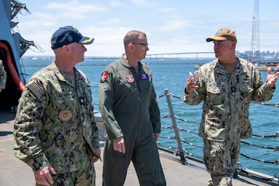 Three military men walk on the deck of a destroyer.