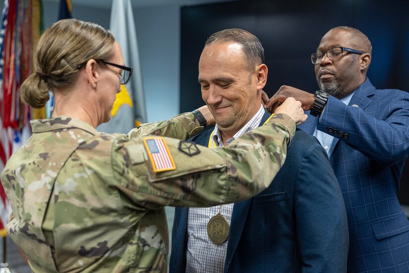 Retired Command Sgt. Maj. Dennis Dodge, U.S. Army Financial Management Command senior quality assurance analyst, receives a U.S. Army Finance Corps Distinguished Member of the Regiment award from Col. Michelle M. Williams, USAFMCOM commander, left and retired Command Sgt. Maj. Gennaro Penn, Finance Corps Association president at the Maj. Gen. Emmett J. Bean Federal Center in Indianapolis June 15, 2026. The Finance Corps designated the first DMR on May 5, 1990, and the program honors individuals whose legacy of landmark contributions and unique acts brings significant credit to the Finance Corps. (U.S. Army photo by Mark R. W. Orders-Woempner)