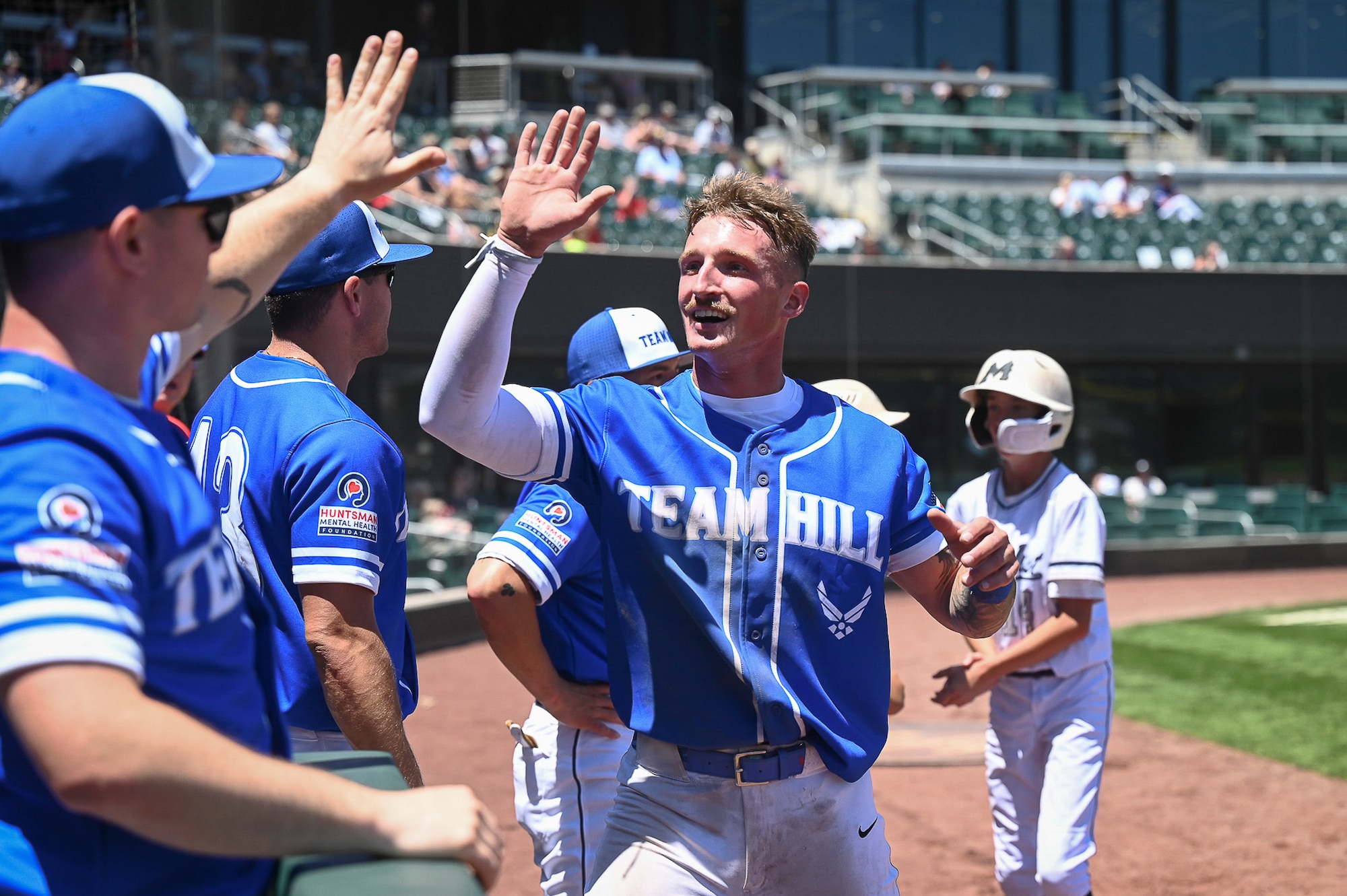 Senior Airman Josh Jamiolkowski smiles and high-fives his military teammates in celebration on the baseball field during an afternoon game