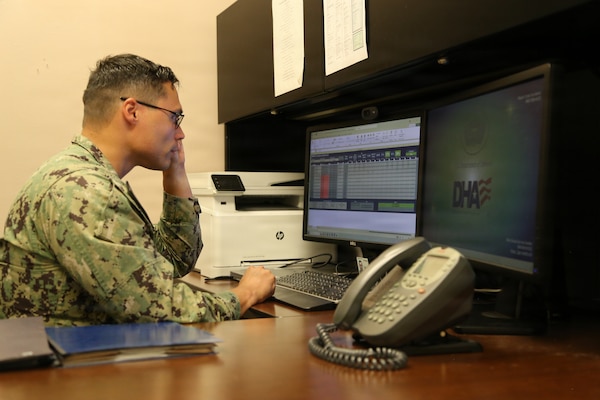 Hospital Corpsman 1st Class Jordan Cooper at his desk in Staff Education and Training, demonstrates the DHMHRSi Excel calculator tool at Naval Health Clinic Lemoore. (Department of War photo by Elaine Heirigs/Released)