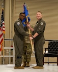 photo of USAF Airmen on a stage, two USAF Airmen are holding a unit flag in between them