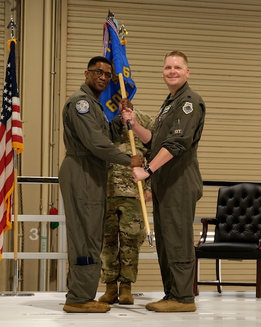 photo of USAF Airmen on a stage, two USAF Airmen are holding a unit flag in between them