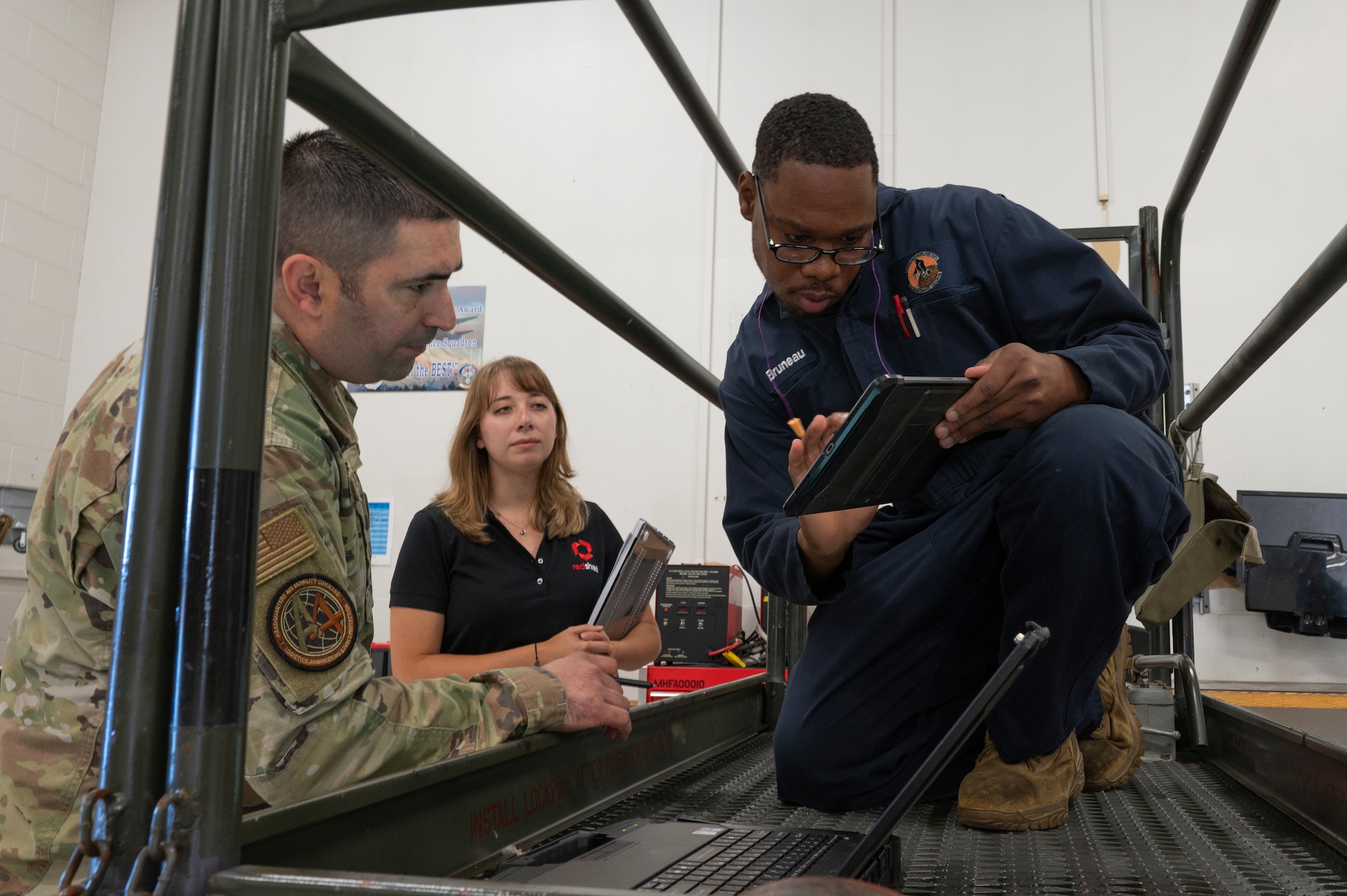 A woman and man stand next to a man crouching on a platform while holding an iPad.