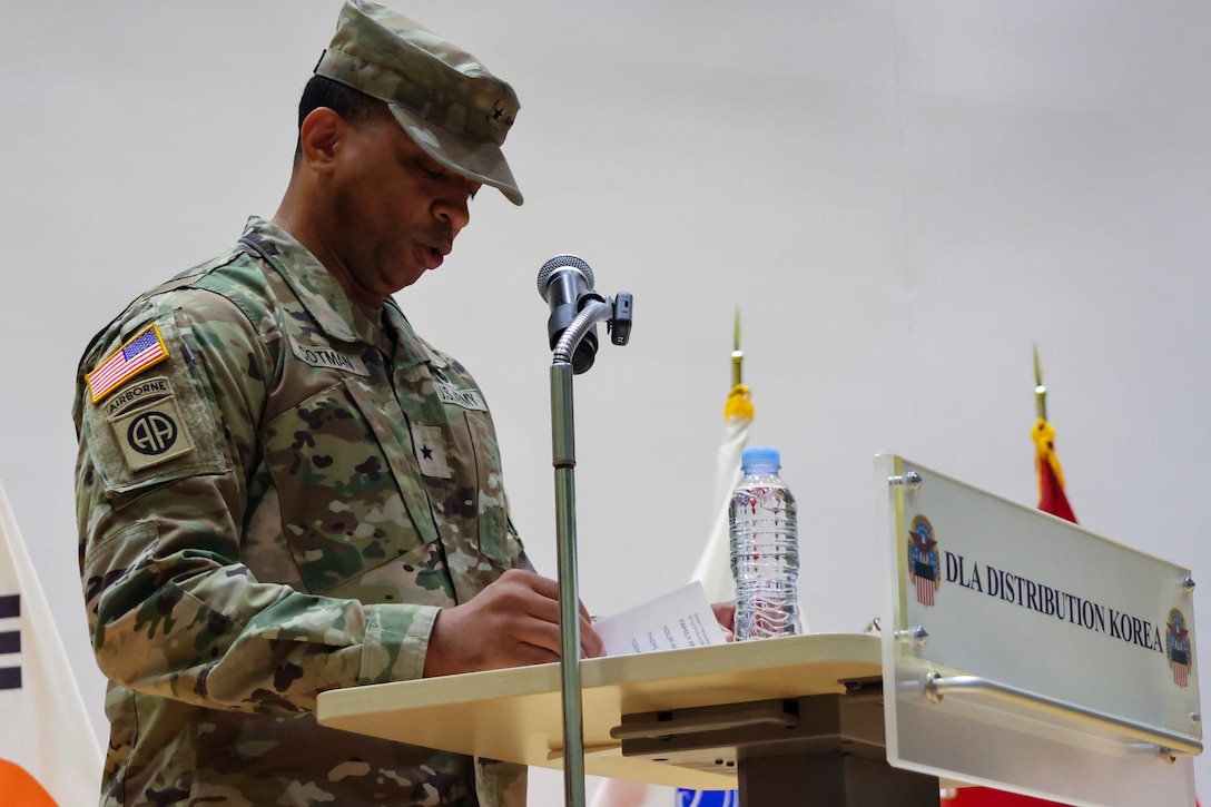 A man wearing a camouflage military uniform stands at a podium speaking.