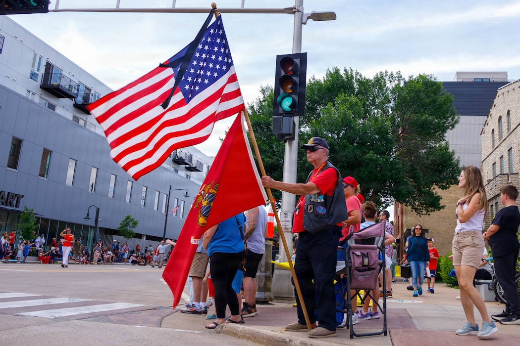 A Retired U.S. Marine Corps Veteran holds the American and Marine Corps flag during the 75th Appleton Flag Day Parade in Appleton, Wisconsin, June 13, 2026. The annual Flag Day Parade is referred to as one of the oldest, largest, Flag Day Parades in the nation with 50,000 patriotic attendees and is led by Marine Forces Reserve Color Guard, Marine Poolees from Recruiting Sub Station Appleton, and the Quantico Marine Band. (U.S. Marine Corps photo by Lance Cpl. Lynsee Avila-Ramirez)