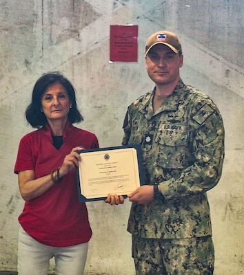 Two people stand holding certificates one is wearing a camouflage military uniform.