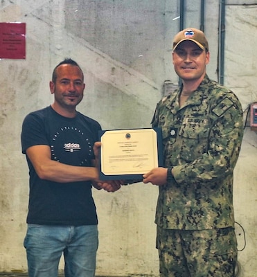 Two people stand holding certificates one is wearing a camouflage military uniform.