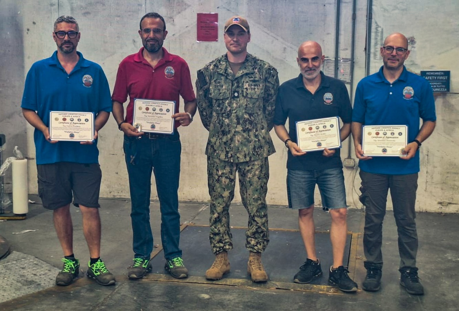 A group of people stand holding certificates one is wearing a camouflage military uniform.
