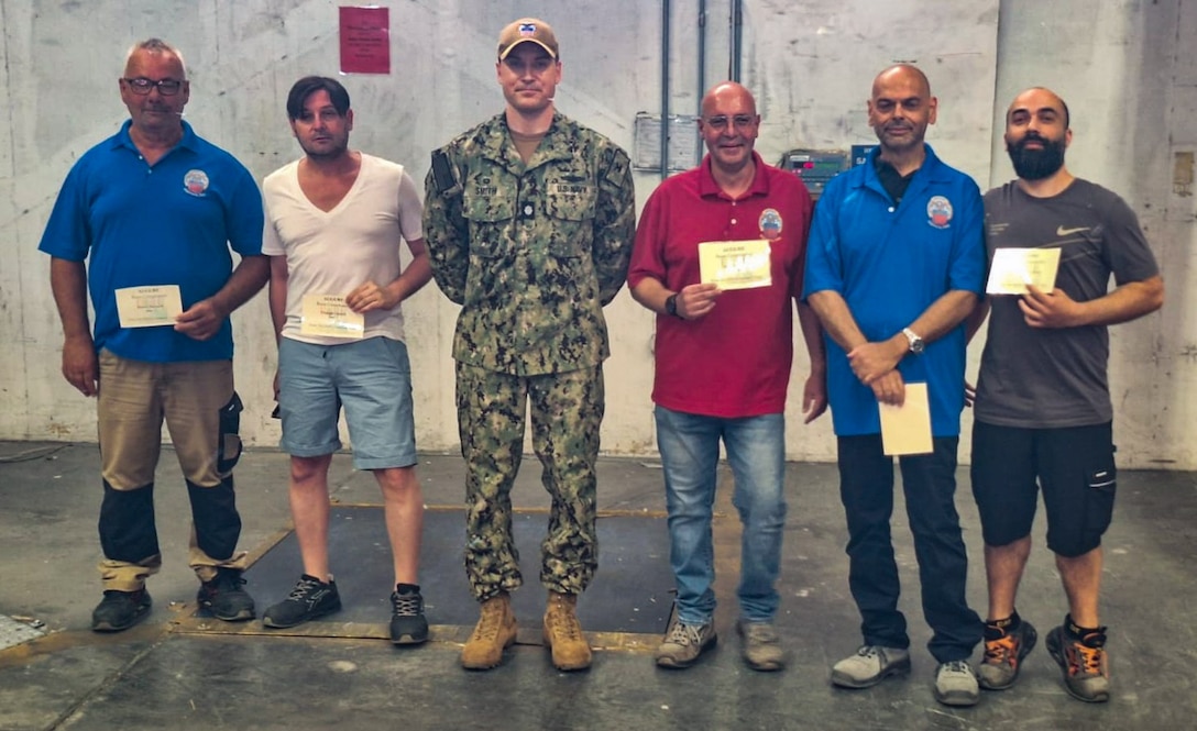 A group of people, one wearing a camouflage military uniform, stand holding certificates.